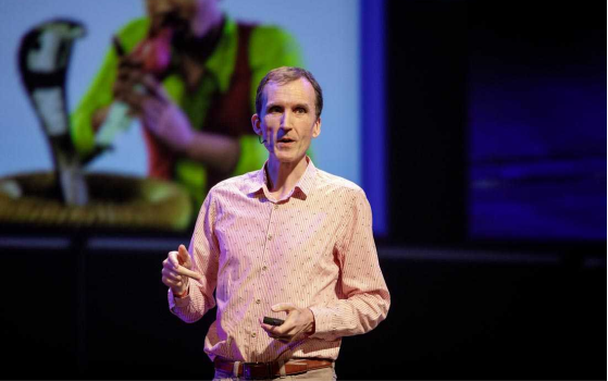 Camp Digital speaker Gerry McGovern speaking on stage. In the background out of focus is a slide on a screen. 