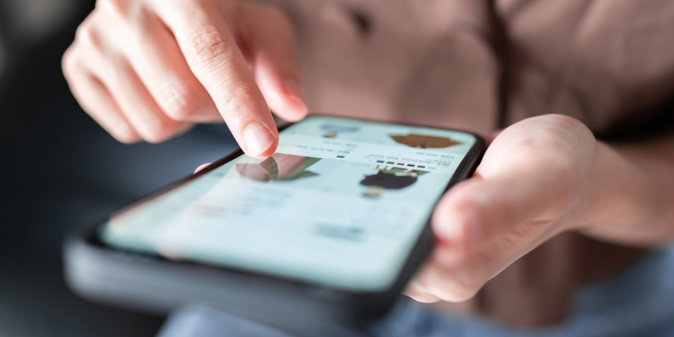 A set of hands typing on a touchscreen mobile screen. Onscreen items in an eCommerce store are visible, though out of focus. 