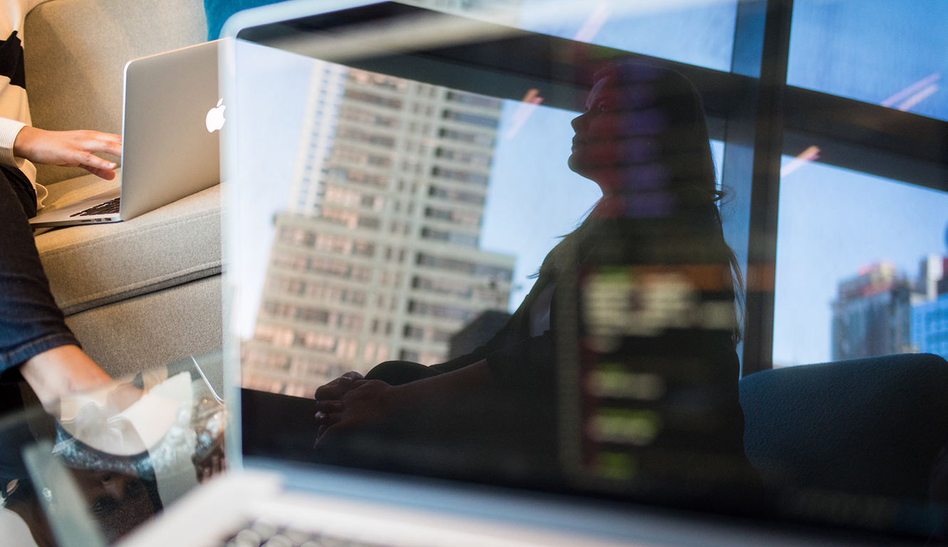 Reflection in laptop screen of woman looking out at the city