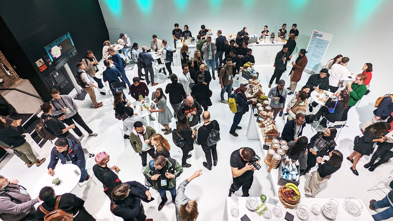 A group of people standing. Some of them are talking and holding plates and some are at a buffet table. 
