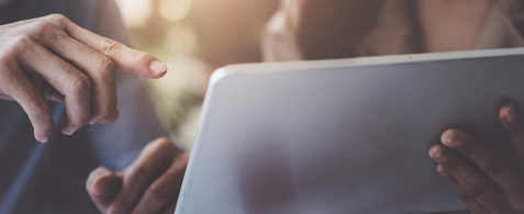A hand holds a tablet, while another points towards the screen