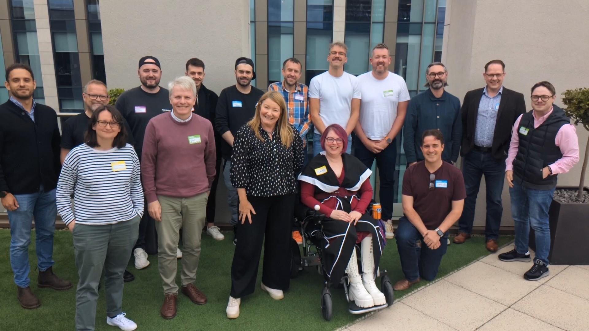 Accessibility roundtable attendees stand on a roof terrace - they're all smiling at the camera