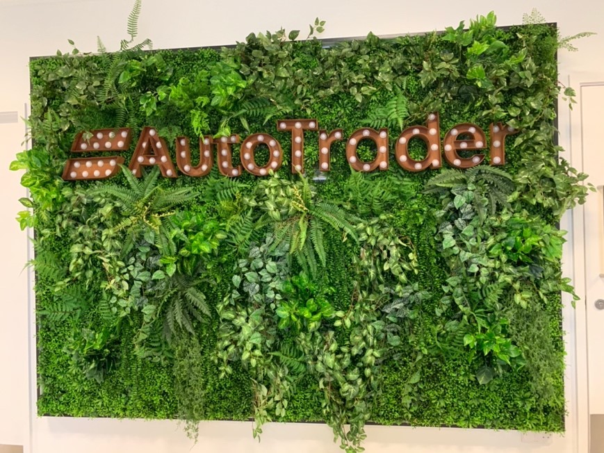 Metallic brown signage reading Auto Trader on a green leafy background