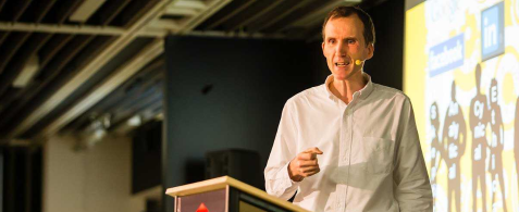Camp Digital speaker Gerry McGovern standing behind a podium and speaking. In the background is a slide. 