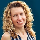 A headshot of Jenny Featherston - a smiling white woman with blonde curly hair and brown eyes.