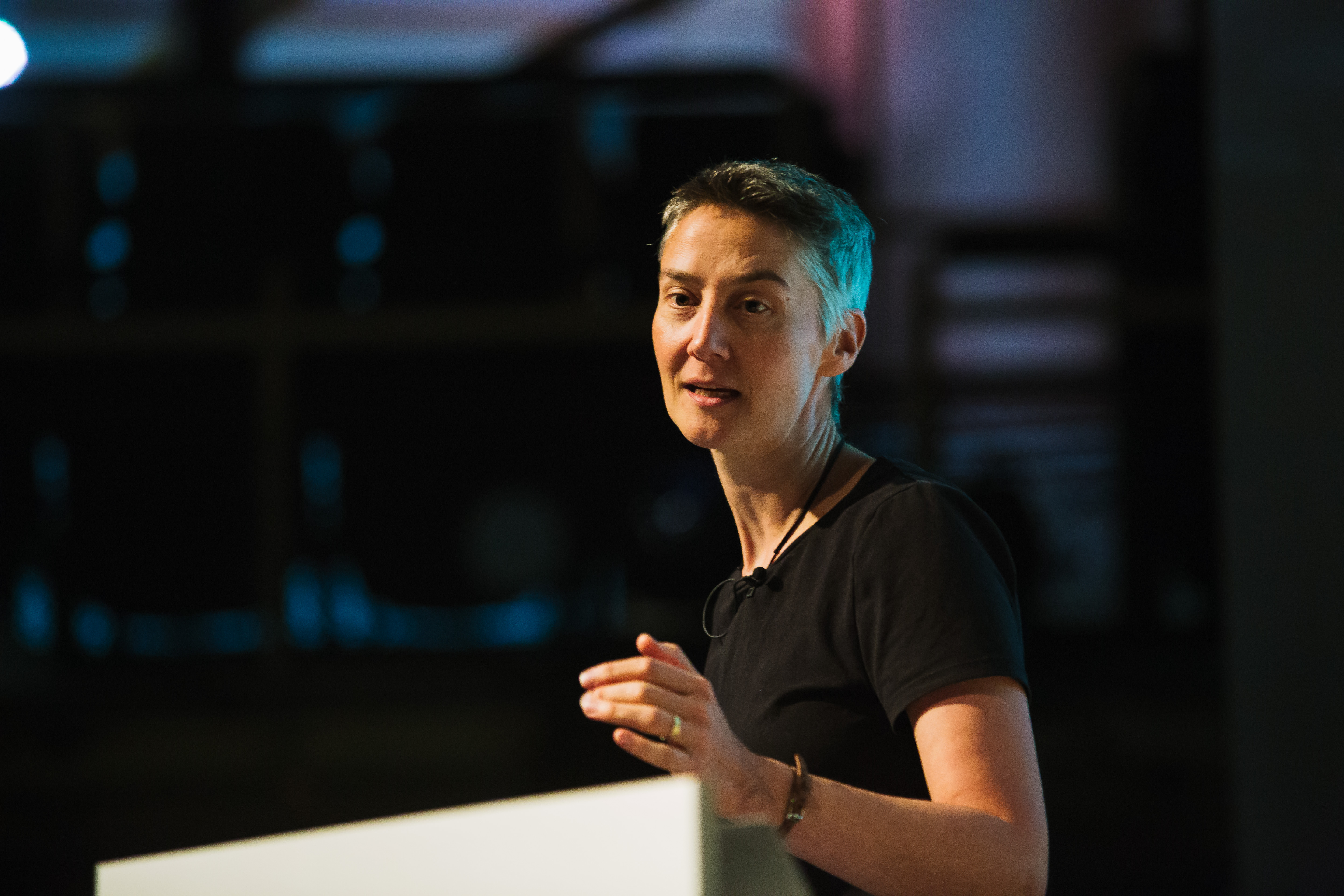 Janet Hughes. A thin white woman with short grey air, gesticulating to the left and looking inquistive. 