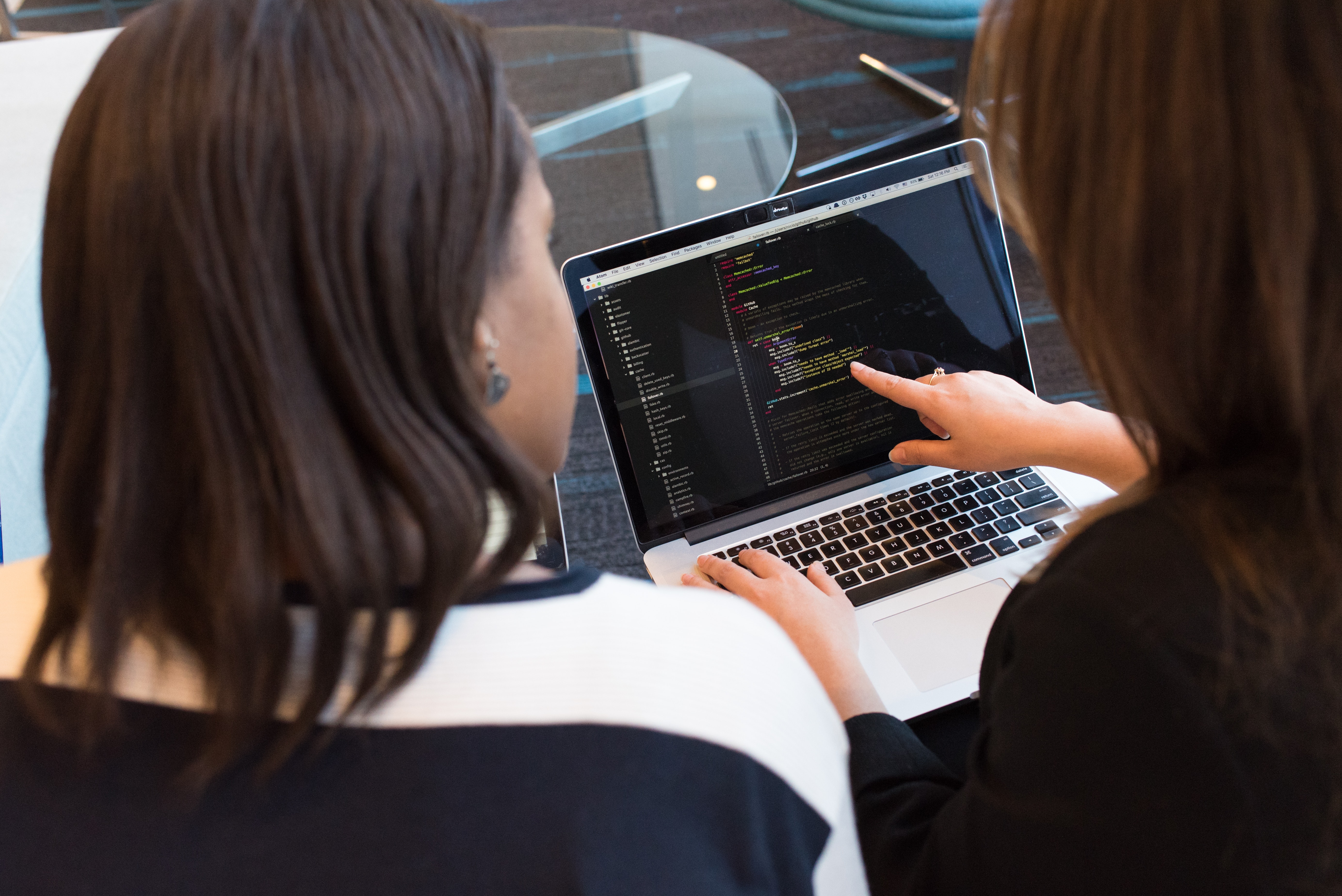 Two women looking at the codeon a Laptop. The woman on the right is pointing at the code