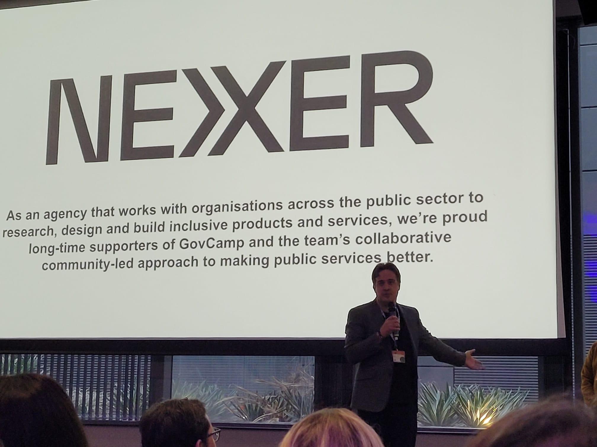 Chris delivers an opening comment to the GovCamp unconference. The Nexer logo can be seen onscreen 
