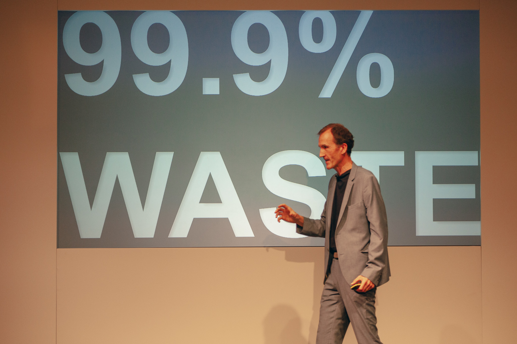 Gerry McGovern onstage at Camp Digital. The slide on screen reads "99.9% waste".