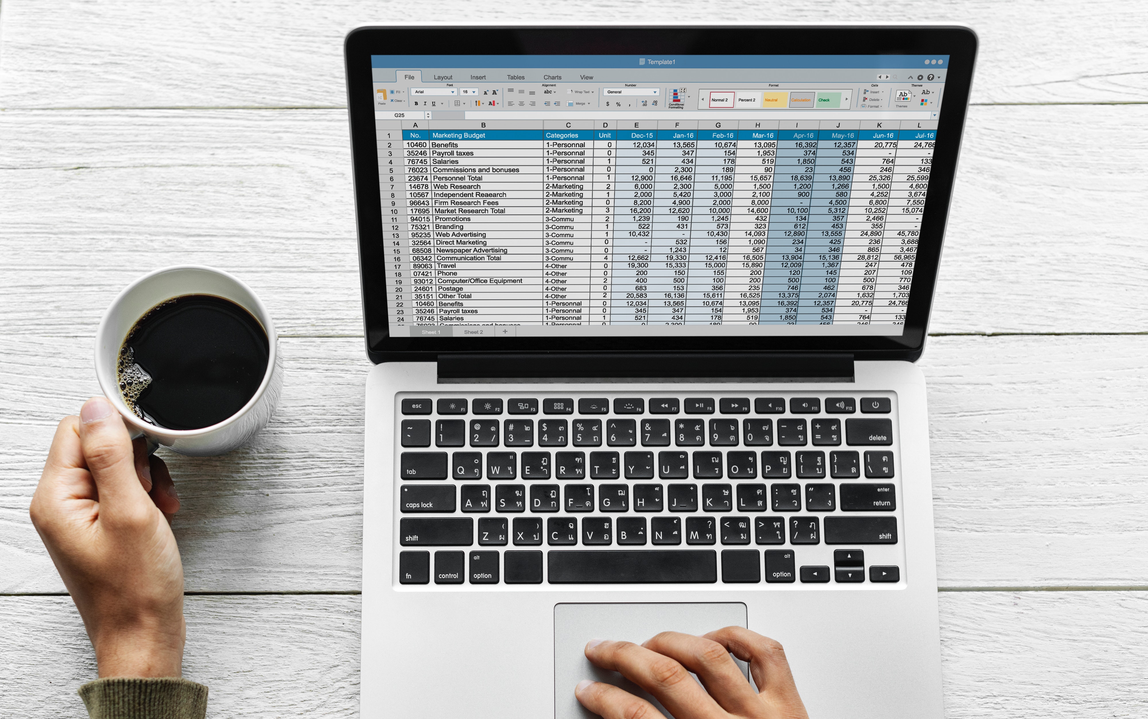 Hands on a trackpad of a laptop and holding a cup of coffee. There is a spreadsheet displaying on the trackpad. 