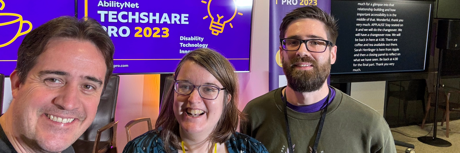 Chris, Emma and Danny from Nexer's accessibility team take a smiling selfie in front of the TechShare Pro 2023 banner
