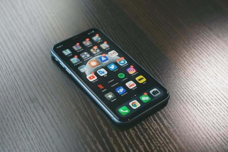 Phone lay upright on a table showing home screen with lots of apps with notifications