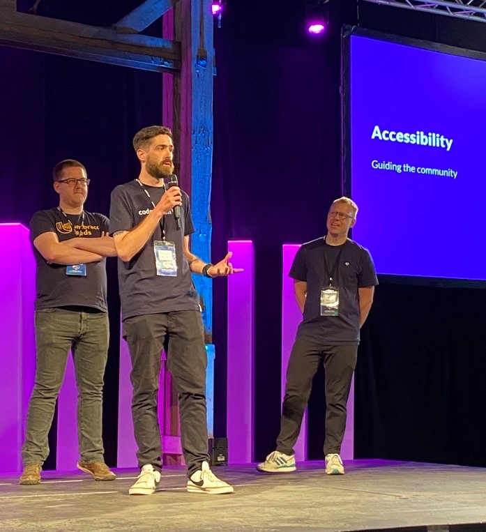 Three people standing on stage with a presentation behind them.