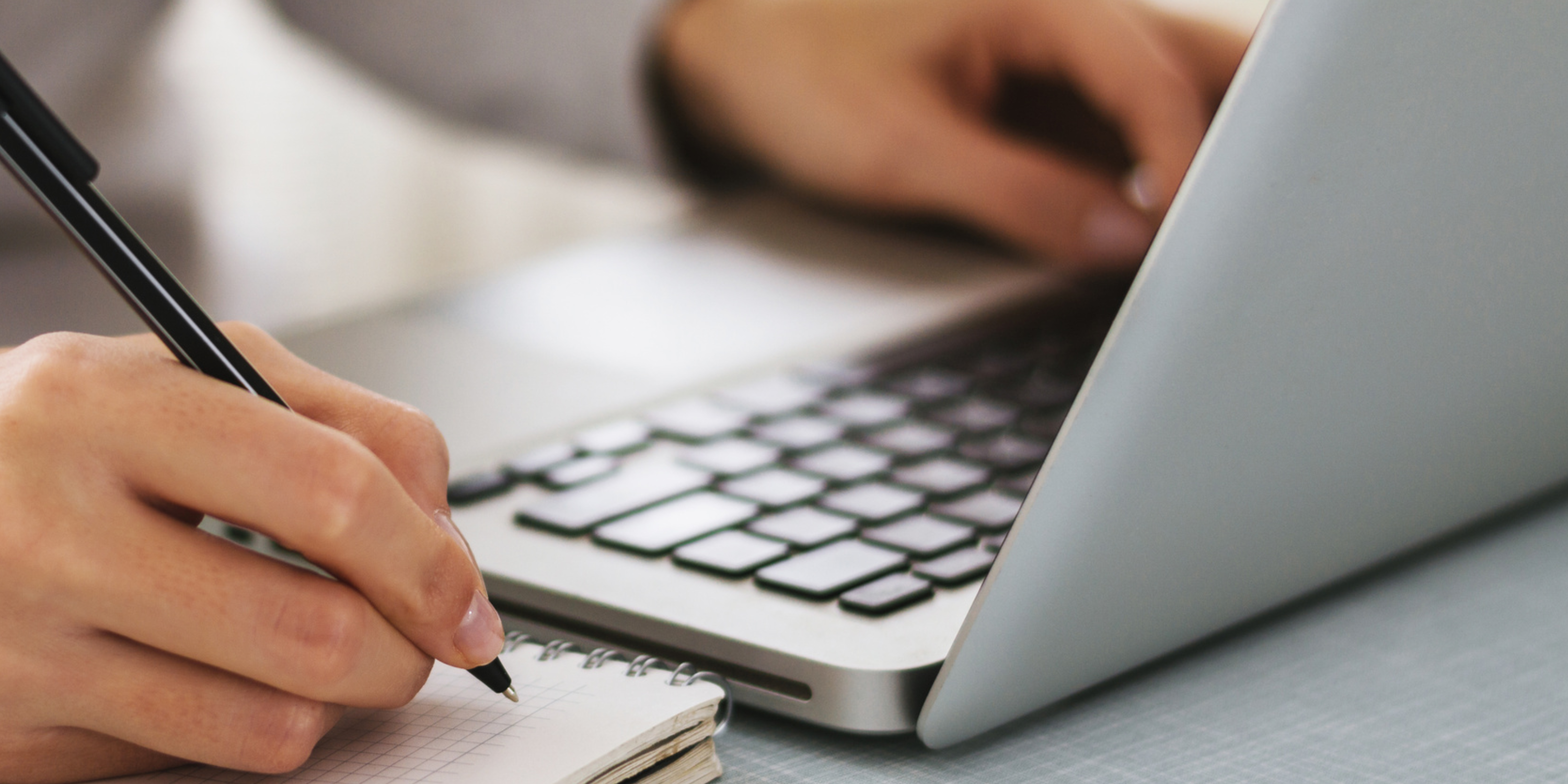 A person writing in a notepad and typing on a laptop