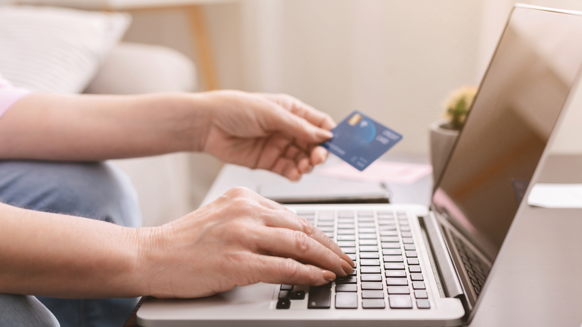 A person typing on a laptop while holding a credit card, suggesting they are inputting card information