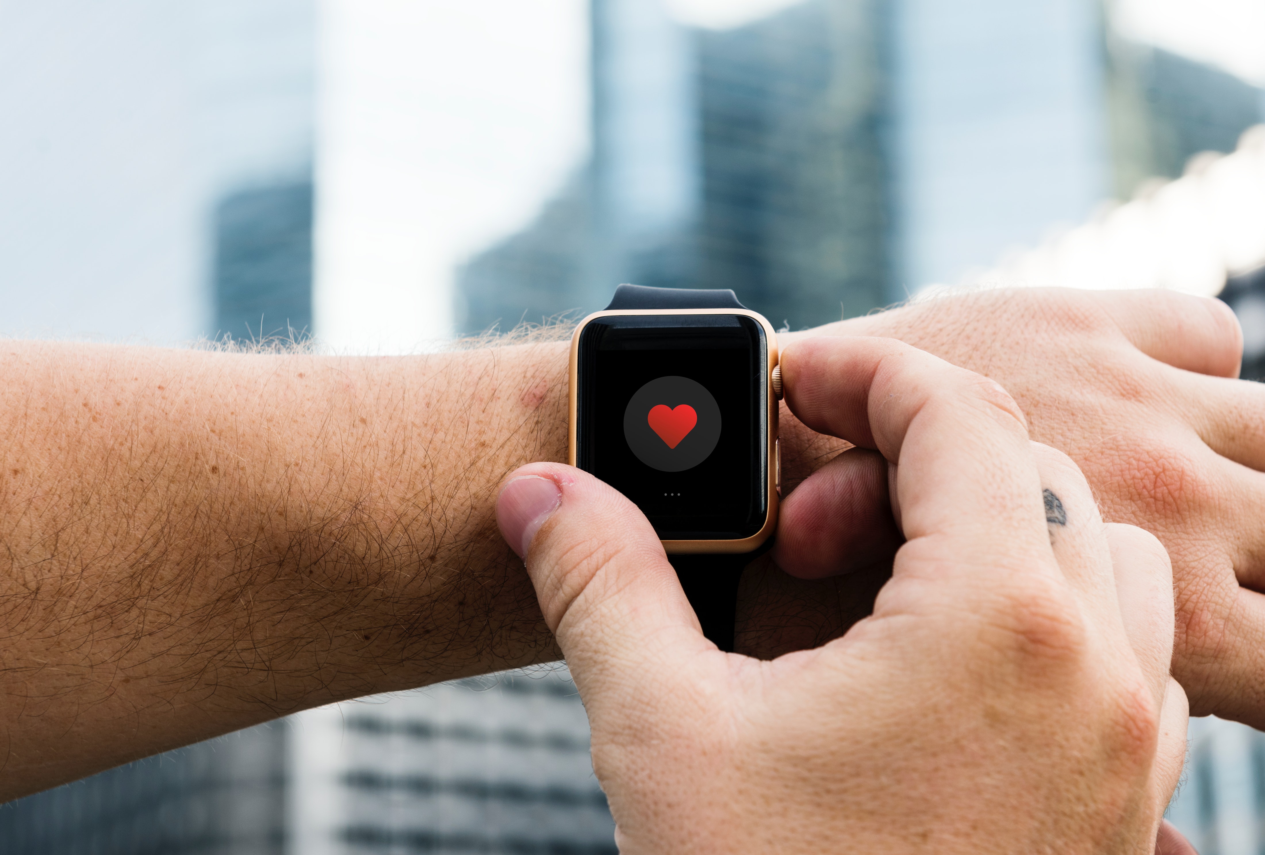 Arm with an apple watch on with a red heart displaying on the watch. 