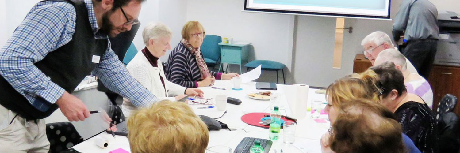 Justin from the Nexer team looks are post it notes on a table. Seated around him are several older people 