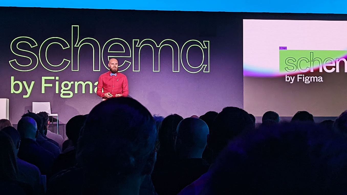 An audience seated in front of a stage with a speaker standing, and a slide reading "schema by Figma"