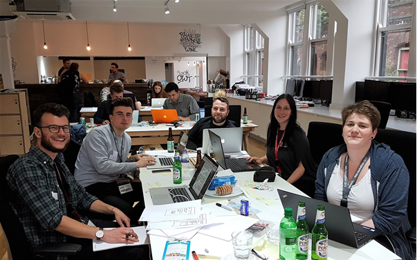 A group of white people sat around a table in an office, with laptops open in front of them.