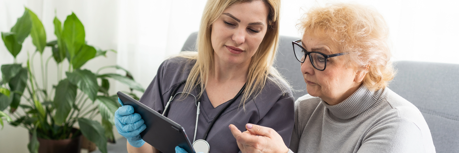 An image of an elderly person and her carer both looking at an ipad with faces of concentration