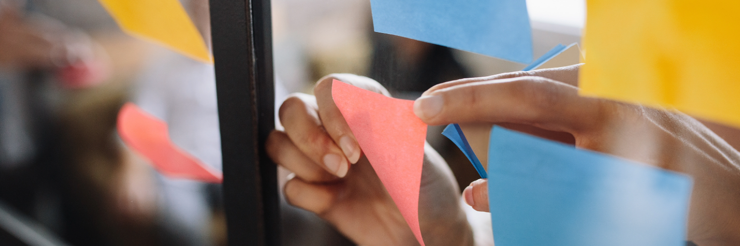 A hand sticks a post it note to a piece of glass which already features post it notes 