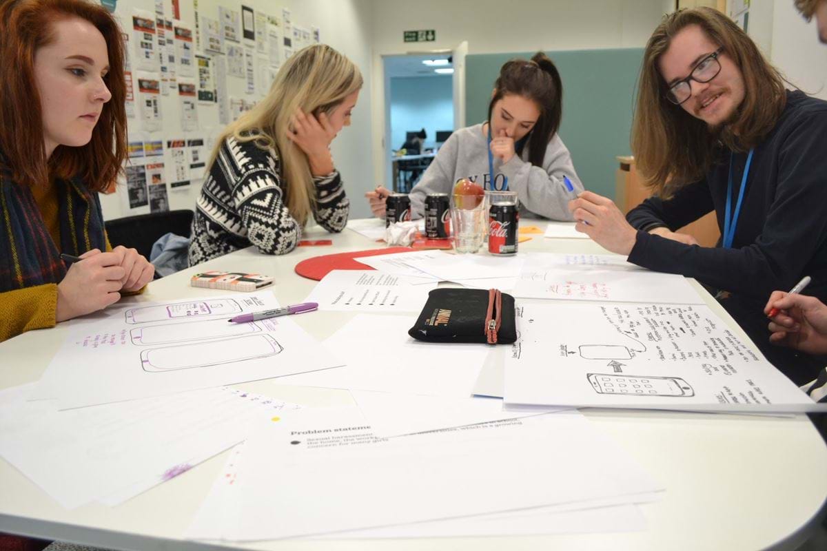 Four white people sat around a table, working and writing on paper.