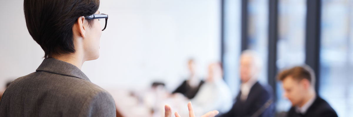 Person with glasses speaking to people sat down in front